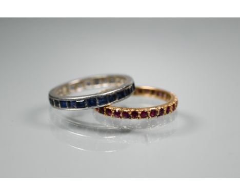 Two eternity rings - one set rubies, yellow metal, size Q 1/2; the other set sapphires, white metal, size R (2) 