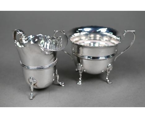 An Edwardian Irish silver cream jug with scroll handle and hoof feet, John Smyth, Dublin 1901, to/w a somewhat similar sugar 