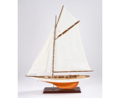 Model depicting a sailing yacht with white and varnished timber hull, on a red gilt line decorated plinth base, 60cm long, 72