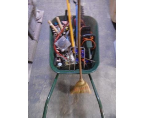 A metal wheelbarrow containing assorted garden tools including electric hedge trimmer.