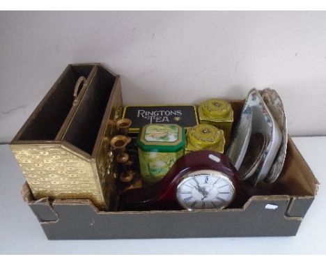 A box containing a brass magazine rack, a pair of candle sticks, a mantel clock, tins etc.