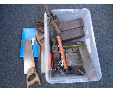 A crate containing vintage saws and tools, blow lamp, woodworking plane.