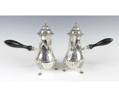 A pair of late Victorian silver chocolate pots, each of pear shape with ebonised side handles and hinged covers, the lower bo