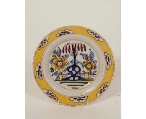 A DELFTWARE PLATE painted in polychrome with floral decoration beside a fence within a yellow and floral border, 18th century