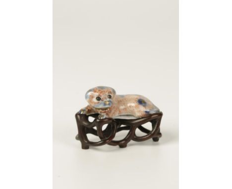 A JAPANESE PORCELAIN NETSUKE in the form of a dog, with underglaze and overglaze decoration heightened in gilt, on a carved w