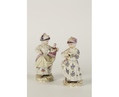 A PAIR OF MEISSEN PORCELAIN FIGURES of two young girls holding toys, wearing bonnets and elaborate dresses, polychrome painte