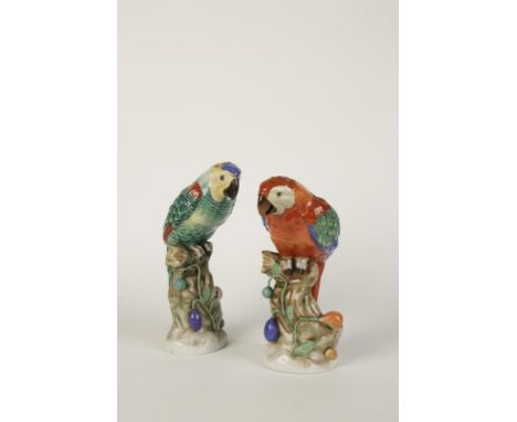 A PAIR OF CONTINENTAL HEREND PORCELAIN PARROTS perched on a tree trunk with entwined vines with berries, decorated in glazed 