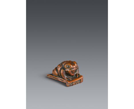 Netsuke einer Kröte auf Dachziegel. Buchsbaum. 19. Jh.Sign.: ShōrinDas fette Tier sitzt auf einem beschädigten Dachziegel, im