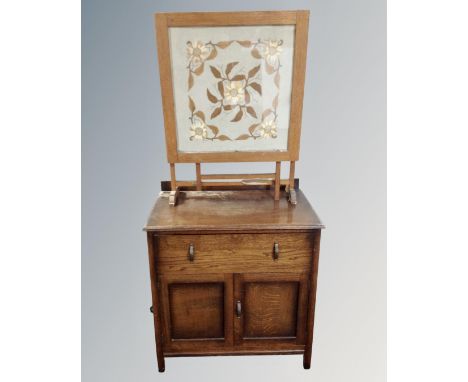 A 1930s oak double door linen cabinet fitted with a drawer, together with a folding tapestry fire screen.