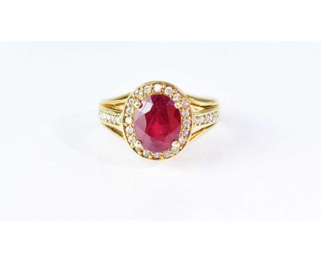 An 18ct yellow gold ring, set with central ruby in a claw mount, surrounded by small diamonds, the shoulders each set with fi