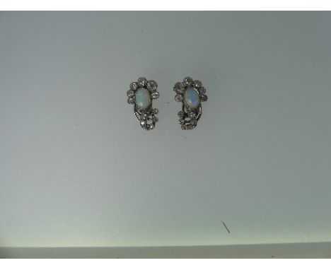 A pair of opal and diamond Ear Clips, the oval opal mounted above six millegrain set graduated diamonds, with three small swi
