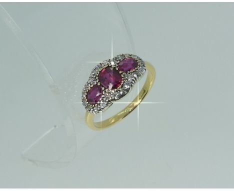 An attractive ruby and diamond three stone Ring, the central oval ruby vertically set, the two others horizontal, millegrain 