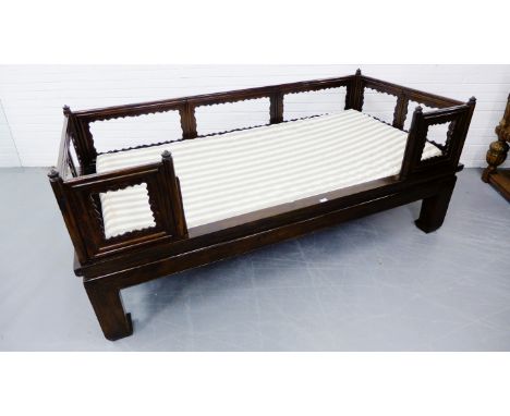 A stained dark wood Chinese day bed with three quarter gallery surround and raised on shaped supports, with striped fabric ma