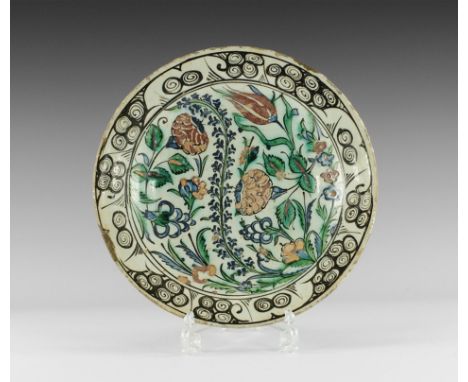 17th century AD. A shallow white-glazed ceramic dish with band of scrolls to the rim, polychrome scene of flowers and leaves 