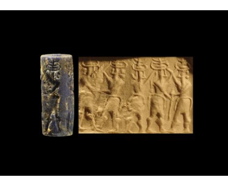 2nd millennium BC. 
A carved lapis lazuli cylinder seal with frieze of standing figures with raised arms wearing horned headd
