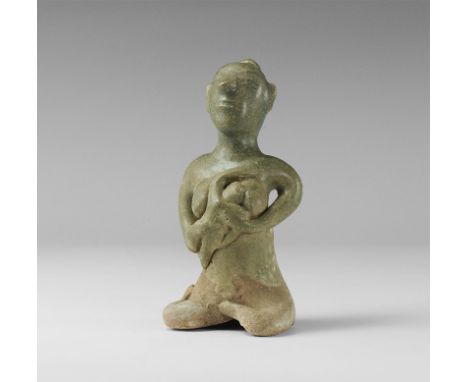 14th-16th century AD. 
A green-glazed ceramic figurine of a nude seated female with bun to the back of the head, suckling a b