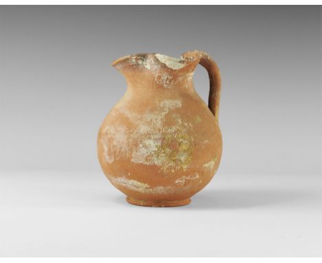 1st-2nd century AD.
A terracotta pitcher with basal plate, globular body, strap handle and trefoil mouth. 415 grams, 15.5cm (
