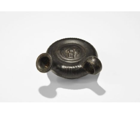 4th century BC. 
A squat blackware ceramic guttos with broad pedestal base, discoid body, loop handle and short spout, ribs t