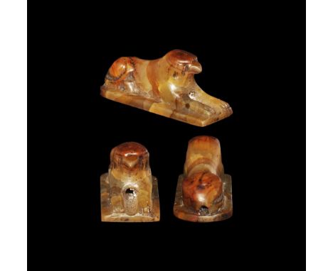 Late Period, 664-332 BC. 
A banded agate amuletic bead of a crouching sphinx with the head of a hawk, on a tongue-shaped base