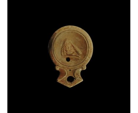 2nd century AD.
A terracotta oil lamp with broad discus, short nozzle with scrolled flanks, recessed discus with facing mask 