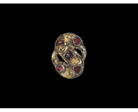 6th century AD. 
A silver S-shaped plate brooch with parcel-gilt chip-carved panels; two discoid eyes with inset garnet clois