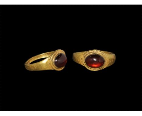 1st century AD.
A narrow round-section gold child's ring with expanding shoulders and discoid plaque, inset garnet cabochon. 