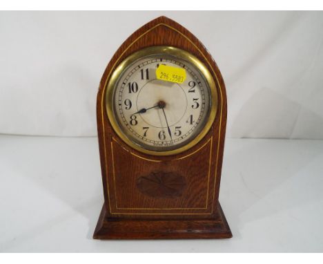 A lancet shaped mantel clock, oak cased with decorative inlaid stringing and marquetry centre piece, Arabic numerals to the c