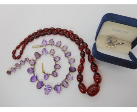 A gilded white metal graduated amethyst necklace with matching brooch, a string of cherry amber coloured beads and a silver a