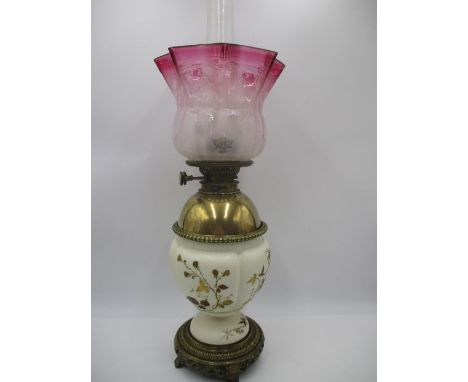 A turn of the Century oil lamp with brass Chinese style base, gilt decorated pottery body and cranberry shade
