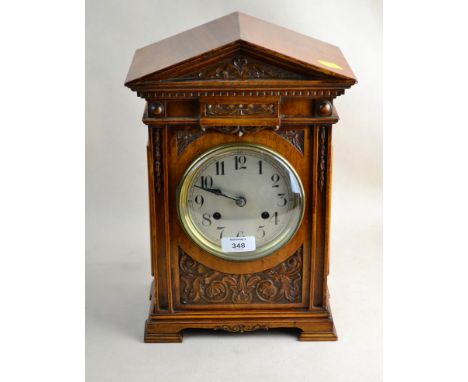 An early 20th/late19th century walnut cased mantel clock, the carved architectural case enclosing a German eight-day gong str