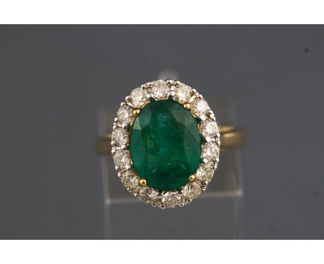 A yellow and white metal cluster ring set with an oval faceted cut emerald of approx. 4.50cts and surrounded by diamonds, app