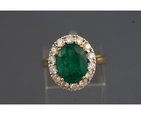 A yellow and white metal cluster ring set with an oval faceted cut emerald of approx. 4.50cts and surrounded by diamonds, app