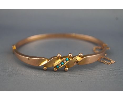 A yellow metal bangle set with turquoise and seed pearls having a push in clasp with fitted safety chain. Hallmarked 9ct gold