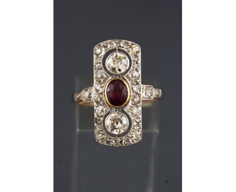 A yellow and white metal panel ring set with a central oval faceted cut ruby. Further set with two old brilliant cut diamonds