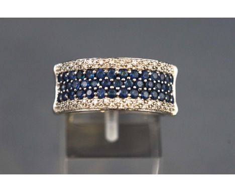 A white metal half hoop dress ring set with three rows of blue sapphires and surrounded by round brilliant cut diamonds. Unte