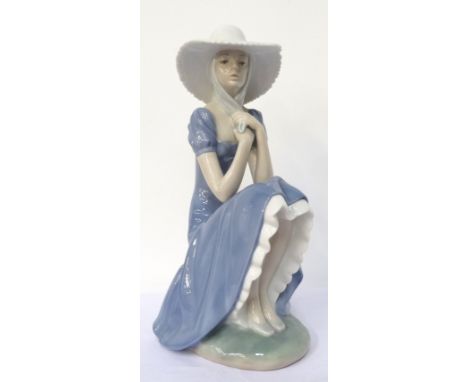 'NAO/LLADRO' FEMALE FIGUREwearing a wide brimmed hat and sitting on a stone wall, printed and incised marks to base, 27.5cm h