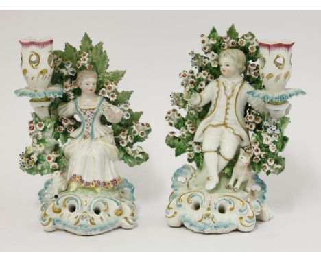 A pair of Paris Candlestick Figures,c.1910, each a seated boy or girl against flowering bocage and with a pierced candle scon