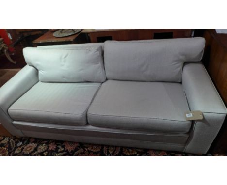 A contemporary designer two seater sofa upholstered in neutral fabric raised on bun feet