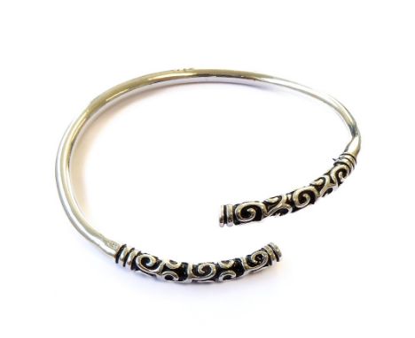 A heavy silver torque bangle; the terminals modelled with scrolls in the niello style