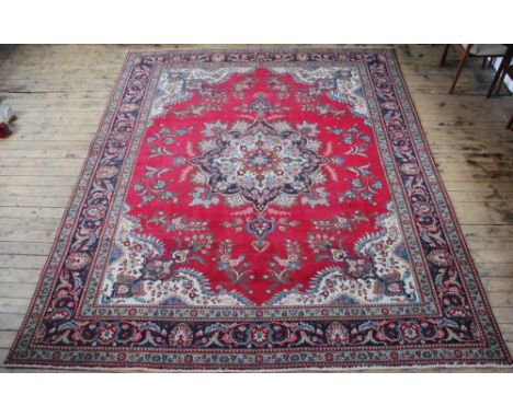 A large Persian wool carpet, worked with a central floral medallion against a red ground, 395cm x 295cm