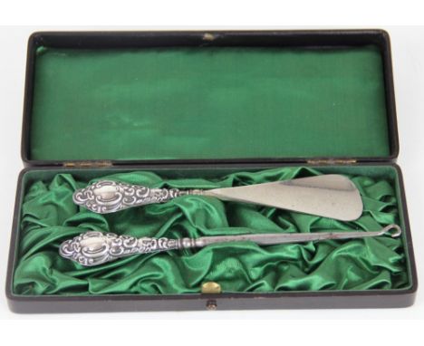An Edwardian silver handled shoe horn and button hook, Chester 1905, each handle embossed with scrolls and foliage, within a 