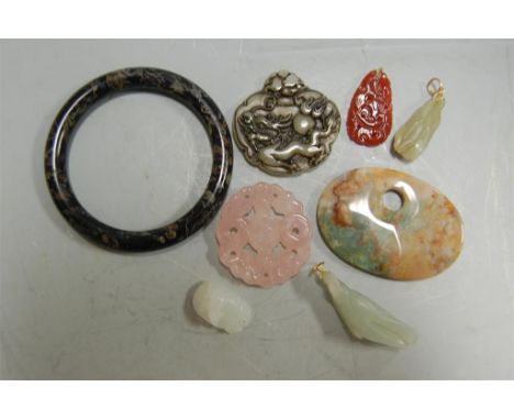 A collection of Chinese carved hardstone pendants to include jade and rose quartz example and a polished hardstone bangle