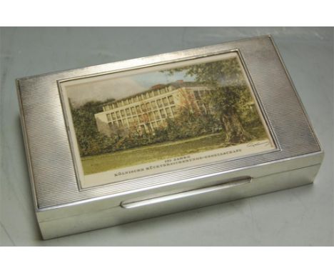 A sterling silver table cigarette box, the lid inset with a panel depicting the Cologne  Reinsurance Company Building