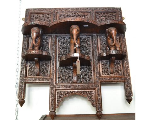 An Indian shelf, ornately carved, and supported by three elephants.