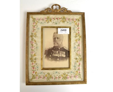 A gilt brass and embroidered photograph frame with a portrait of a senior military gentleman.