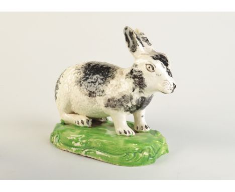 A rare Staffordshire figure of a crouching rabbit, decorated with sponged black glaze on a green mound. Length 15cm. Circa 18