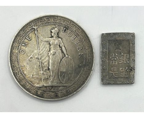 A trade dollar, 1909, and a small Chinese silver coloured ingot (2)