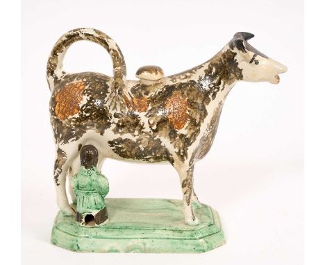 Prattware cow creamer, circa 1820, with ochre and brown decoration, on a green stepped base with milkmaid, 14.5cm high