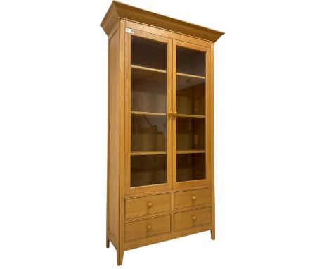 Tall light oak display cabinet, fitted with two glazed doors enclosing three adjustable shelves over four cock-beaded drawers