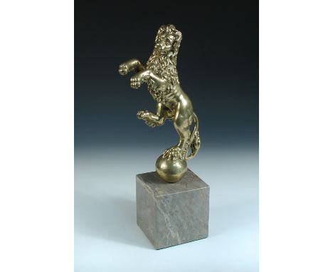 A polished bronze figure of a rampant lion, his head turned to one side as he stands with one foot on a ball, 34cm (13.25 in)